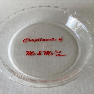 May include: A clear glass pie plate with a red inscription that reads "Compliments of Mc & Mc Port Alberni".