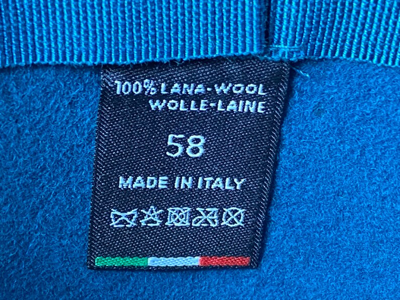 May include: A black label with white text that reads "100% Lana-Wool Wolle-Laine 58 Made in Italy". The label also has a care tag with symbols and an Italian flag.
