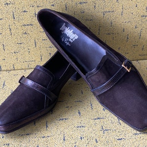 May include: Pair of brown suede heeled loafers with a buckle strap and a square toe. The shoes are labeled "Inglewood by Rampage".