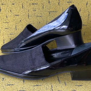 May include: A pair of black heeled shoes with a pointed toe. One shoe is made of a black fabric with a textured pattern, while the other is made of patent leather.