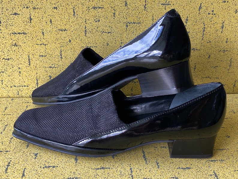 May include: A pair of black heeled shoes with a pointed toe. One shoe is made of a black fabric with a textured pattern, while the other is made of patent leather.