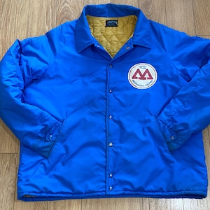 May include: A vibrant blue vintage jacket with a yellow quilted lining. The jacket has a button-up front, a collar, and a chest patch with the text "SAFETY TEAM MECHANICAL HOLDING".