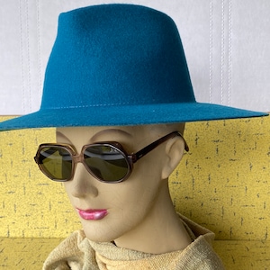 May include: A teal felt fedora hat with a wide brim and a brown pair of sunglasses.