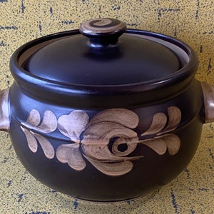 May include: A black ceramic casserole dish with a lid. The dish features a floral design in a light brown colour.