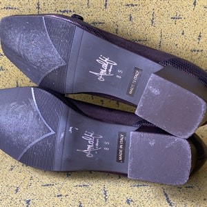 May include: A pair of black suede heeled shoes with a buckle detail. The shoes are size 8.5 and say "Amalfi" on the sole. The shoes are made in Italy.