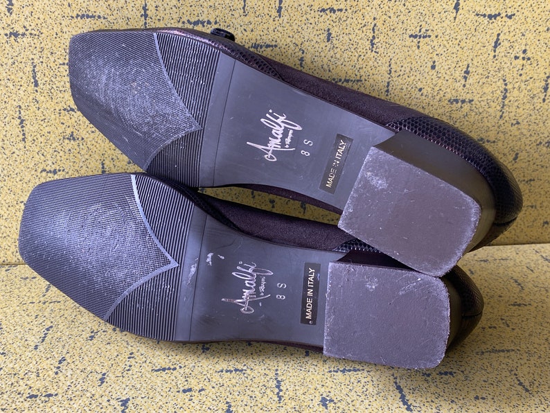May include: A pair of black suede heeled shoes with a buckle detail. The shoes are size 8.5 and say "Amalfi" on the sole. The shoes are made in Italy.