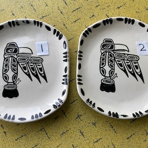 Pode incluir: Dois pratos de cerâmica branca com borda preta e um desenho de pássaro estilizado em preto e branco. Os pratos são numerados 1 e 2.