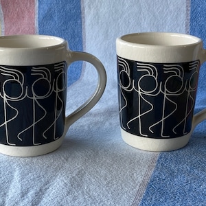 Peut inclure: Deux tasses en céramique blanche avec des motifs de personnages en bâtonnets noirs et blancs. Les personnages dansent et ont un fond noir.
