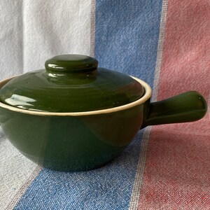 Op de afbeelding: Een groene keramische ovenschaal met een deksel en een handvat. De schaal heeft een witte rand.