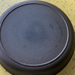 May include: A black cast iron skillet, marked "MADE IN USA" and "NO. 10 12 1/8 IN" (approx. 30.8 cm). The pan has a circular cooking surface with a raised rim and two small handles. The skillet is designed for cooking.