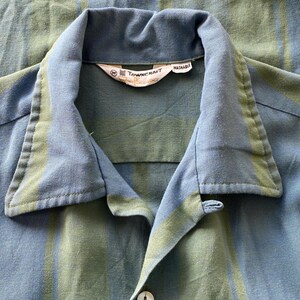 May include: Close-up of a blue and green striped button-down shirt. The shirt has a classic collar and a button closure. The tag reads "TOWN CRAFT WASHABLE". The fabric has a soft, textured appearance.