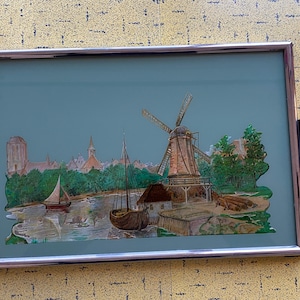 May include: A vintage serving tray with a silver frame and a green background. The tray features a paper cutout scene of a windmill, boats, and a small town.