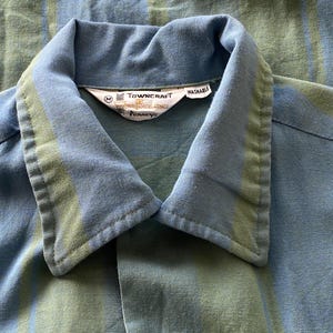 May include: Close-up of a blue and green striped shirt collar. The collar is a lighter blue with a green stripe. The shirt has a tag that reads "Towncraft" and "Washable".