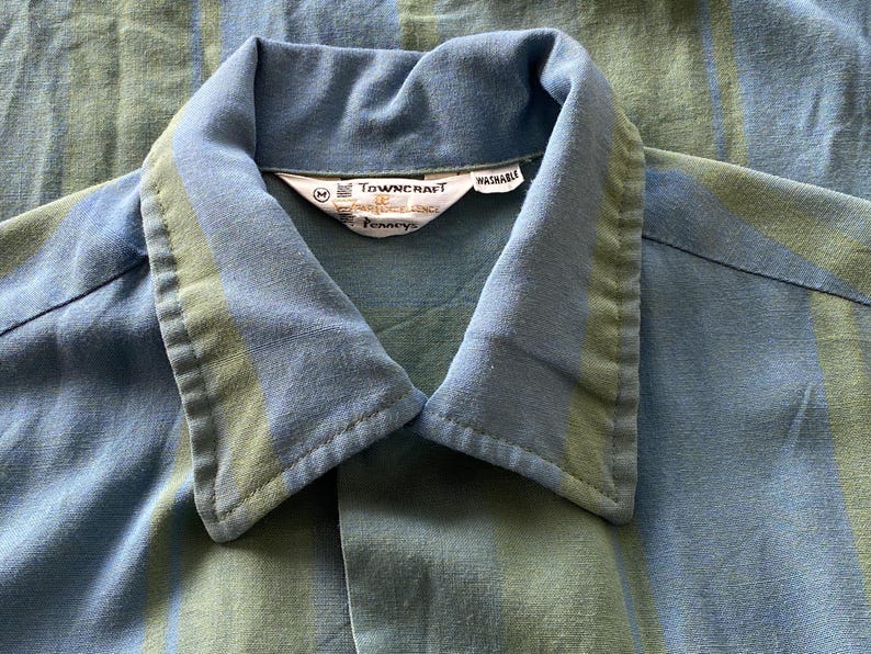 May include: Close-up of a blue and green striped shirt collar. The collar is a lighter blue with a green stripe. The shirt has a tag that reads "Towncraft" and "Washable".