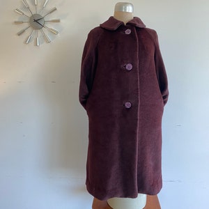 May include: A long, brown coat with a collar and three buttons. The buttons are a light purple color.