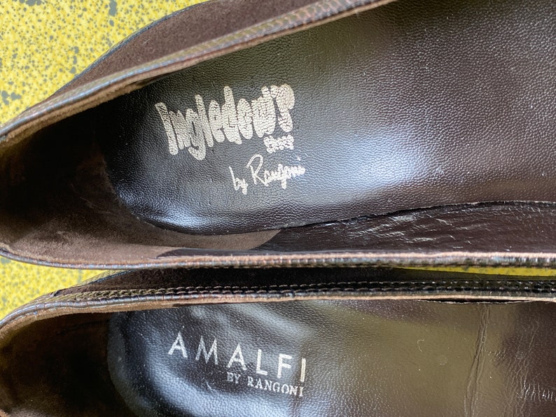 May include: Close-up of the inside of two brown suede shoes. The top shoe has the text "Ingledow Shoes by Rangoni" printed on the insole. The bottom shoe has the text "Amalfi by Rangoni" printed on the insole.