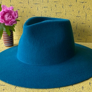 May include: A teal blue fedora hat with a wide brim. The hat is made of felt and has a smooth finish.