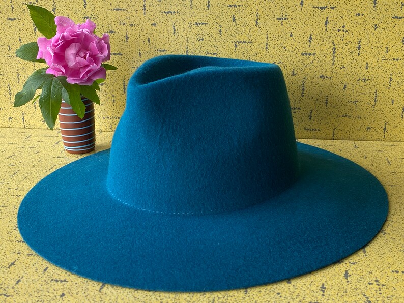 May include: A teal blue fedora hat with a wide brim. The hat is made of felt and has a smooth finish.