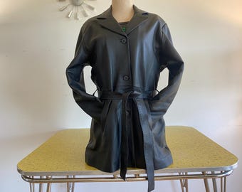 Könnte beinhalten: Ein schwarzer Ledermantel mit Gürtel und Knopfleiste. Der Mantel hat eine lange, fließende Silhouette und ein klassisches Design.