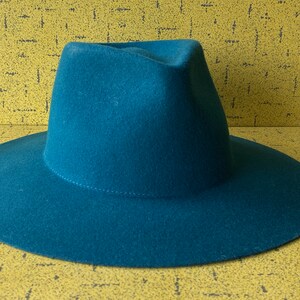 May include: A teal blue fedora hat with a wide brim.