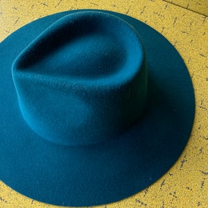 May include: A teal blue fedora hat with a wide brim.