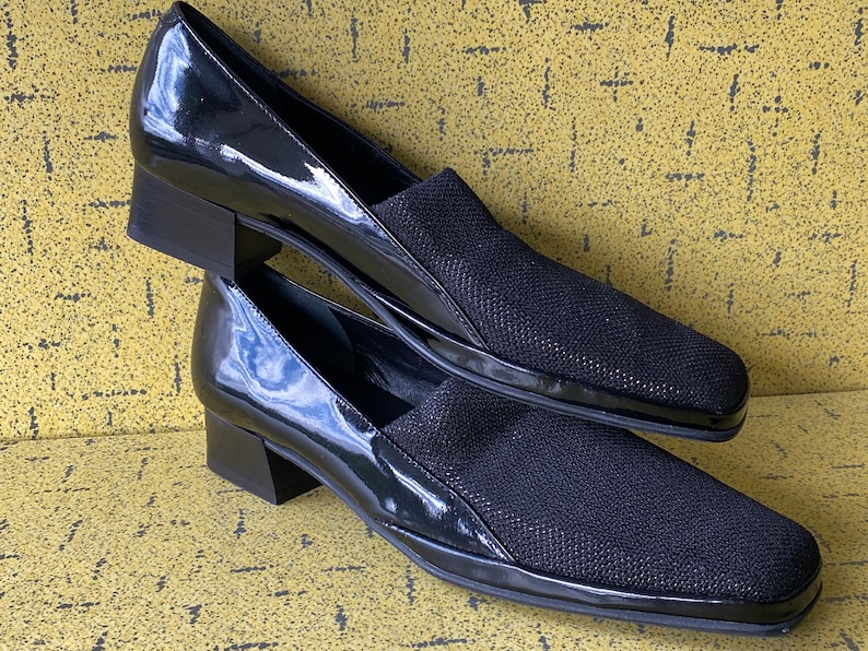 May include: A pair of black heeled shoes with a patent leather toe and a black fabric upper.