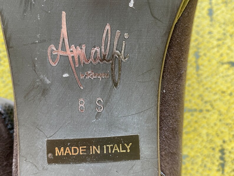 May include: Close-up of the bottom of a brown suede shoe with the label "Amalfi by Rangoni" and "Made in Italy" printed on the sole. The shoe size is 8S.