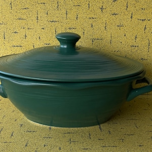 Peut inclure: Un plat à casserole en céramique vert foncé avec un couvercle assorti. Le plat a deux poignées et un bouton sur le couvercle. La surface présente un motif texturé et strié. Le plat est probablement utilisé pour la cuisson et le service des aliments.