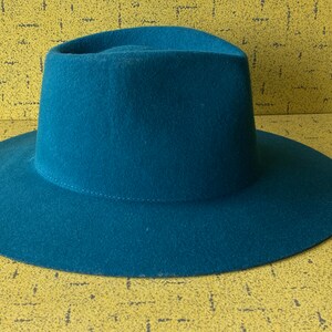 May include: A teal blue fedora hat with a wide brim.