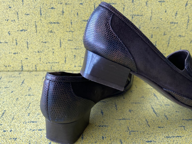 May include: A pair of brown heeled shoes with a snakeskin pattern. The shoes have a low block heel and a pointed toe.
