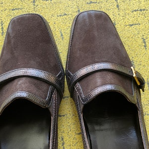 May include: A pair of brown suede shoes with a buckle strap and a snakeskin-like trim.