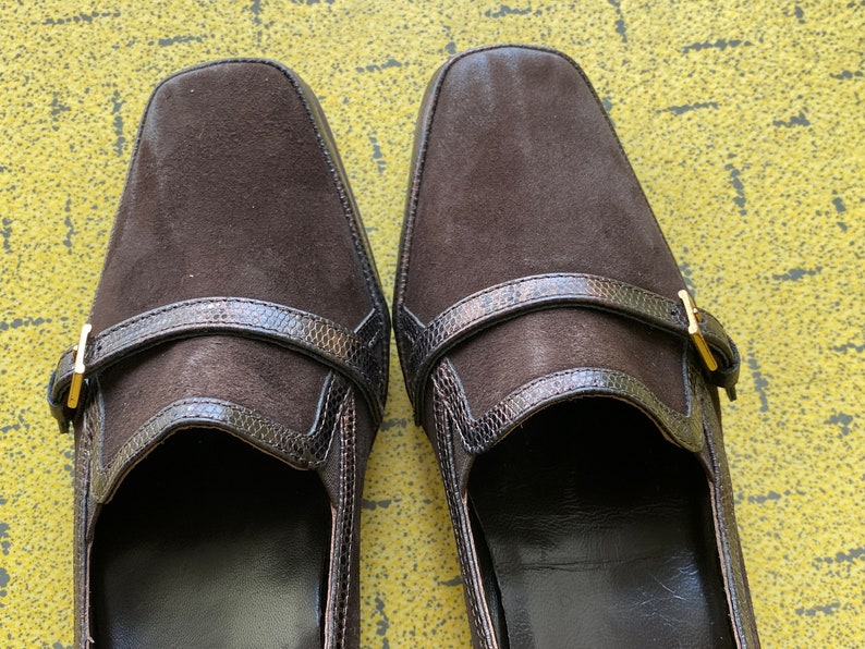 May include: A pair of brown suede shoes with a buckle strap and a snakeskin-like trim.