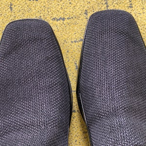 May include: A pair of black leather shoes with a textured surface. The shoes have a pointed toe and a low heel.