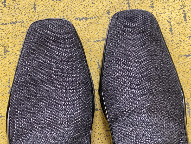 May include: A pair of black leather shoes with a textured surface. The shoes have a pointed toe and a low heel.