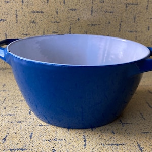May include: A blue cast iron casserole dish with a white interior. The dish has two handles and a flared shape. This cookware is suitable for baking and serving. The dimensions are approximately 25 cm in diameter.