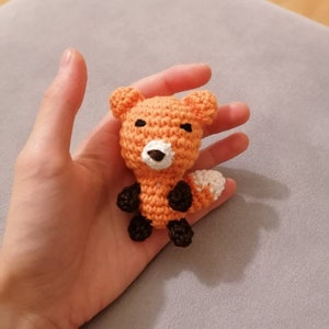 Könnte beinhalten: Ein kleines gehäkeltes Fuchsspielzeug mit orangefarbenem Fell, weißen Akzenten am Schwanz und schwarzen Augen und Füßen.