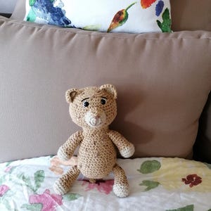 Può includere: Un peluche all'uncinetto che ricorda un leopardo marrone e beige con occhi neri. L'animale è seduto su un copriletto con motivo floreale.