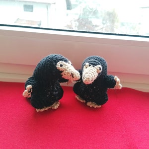 Könnte beinhalten: Zwei schwarze und weiße gehäkelte Stofftiere in Form eines Nifflers aus der Harry-Potter-Reihe. Die Nifflers schauen sich an und berühren sich mit ihren Schnäbeln.