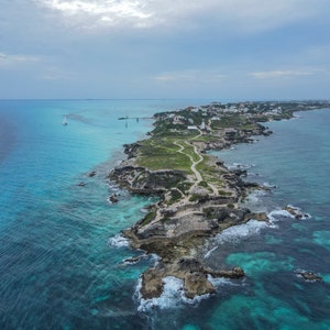 May include: Aerial view of a small island with a rocky coastline and a path leading through the center. The island is surrounded by turquoise blue water and whitecaps.