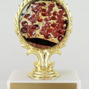 May include: Gold-colored trophy with a round base and a laurel wreath design. The center of the trophy features a picture of a pepperoni pizza.