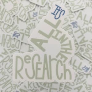 May include: A white sticker with the text "It's All in the Research" in a green-grey color. The text is in a circular shape with the word "It's" in blue at the top.