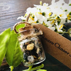 May include: A small glass jar with a cork stopper filled with herbs, crystals, and dried flowers. The jar is tied with twine and has a tag that reads "Nightmare Chaser Spell".
