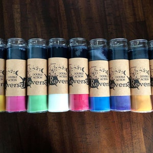 May include: Ten glass candle jars with black wax and brown labels. The labels have a black cauldron and moon design with the text "Double Action Reversal". The candles are in various colors, including yellow, pink, green, white, red, blue, purple, orange, and brown.