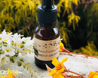 May include: A small brown glass bottle with a black dropper top and a label that reads "Salem's Cauldron Shop Prosperity & Abundance". The bottle is sitting on a white surface with yellow flowers.