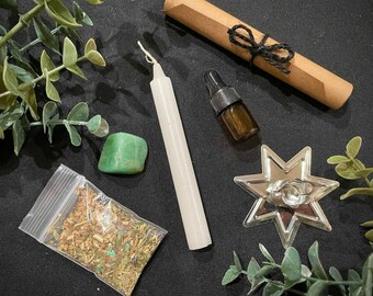 May include: A white candle, a small bottle of essential oil, a green crystal, a small bag of dried herbs, and a silver star-shaped candle holder on a black background.