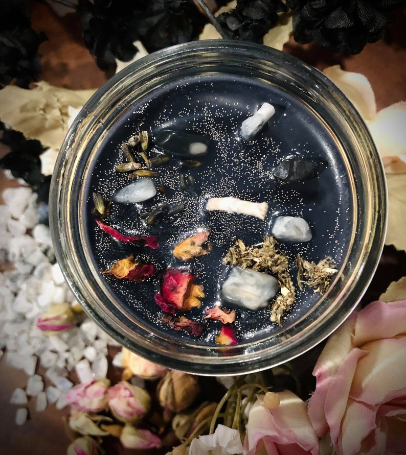 May include: A black candle with embedded crystals, dried herbs, and rose petals in a clear glass jar.