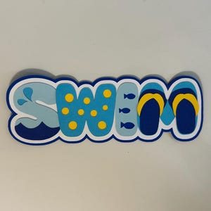 May include: A layered paper cutout sign spelling the word SWIM in blue, light blue, and yellow. The letter S features a water splash, the W has yellow polka dots, the I includes small fish icons, and the M is shaped like a pair of flip-flops.