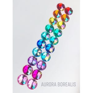 May include: A rainbow assortment of iridescent round glass gems with a faceted design. The gems are arranged in a line from red to purple. The text "AURORA BOREALIS" is printed below the gems.