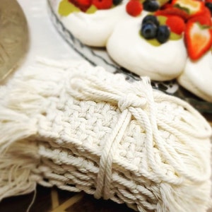 Peut inclure: Un ensemble de quatre dessous-de-verre en crochet blanc avec des franges. Les dessous-de-verre sont empilés les uns sur les autres et liés ensemble par un cordon blanc.