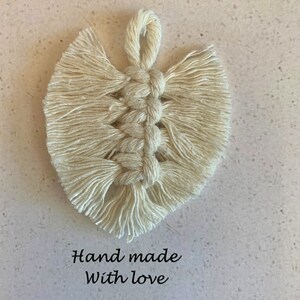 May include: A white macrame heart-shaped wall hanging with the text "L'atelier Okad" and "Hand made with love" on a beige background.